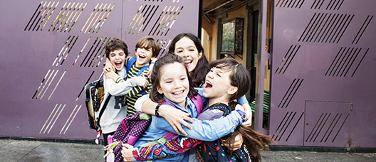 Grupo de niños y niñas a la salida de la escuela abrazándose y riendo