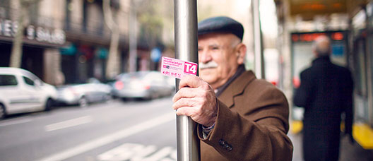 Man waiting for the bus at a bus stop, holding the Pink Card in his hand 