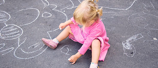Girl sitting on the ground drawing with a chalk on the pavement 