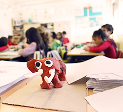 Elefante de plastilina sobre una mesa y al fondo los alumnos dando clase