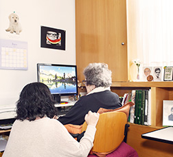 Mujer sentada junto a otra mayor de 65 años mirando el ordenador 