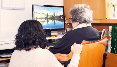 Una dona jove ajuda una dona gran a fer servir un ordinador. 