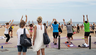 Dues dones miren com un grup de persones fa ioga a la platja 