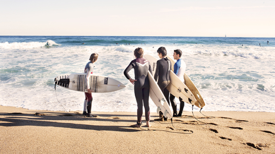 Group of surfers at the shore with surfboards under their arms 